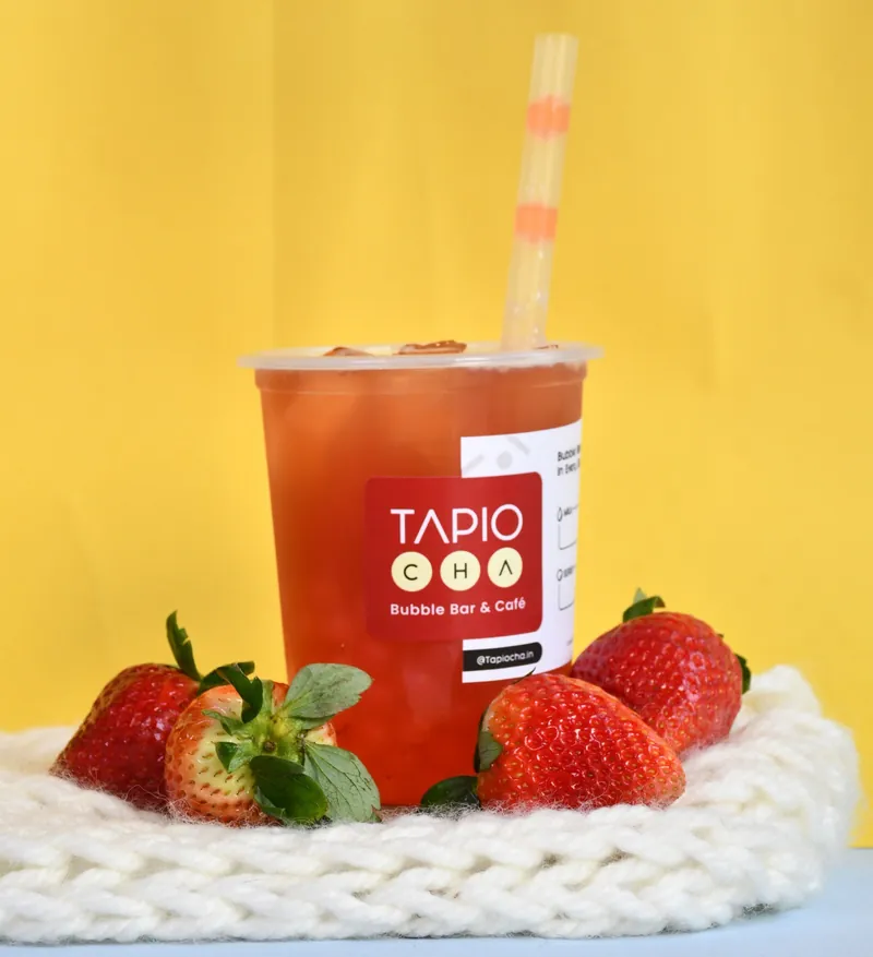 Strawberry fruit tea in a Tapiocha cup with fresh strawberries on a yellow backdrop